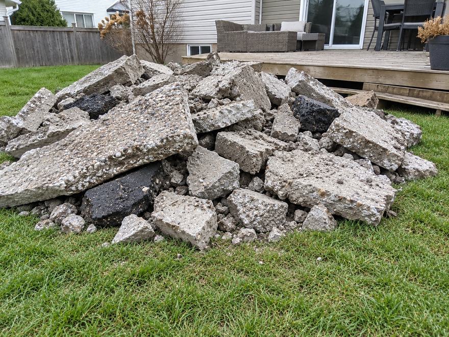 Heap of broken concrete slabs and asphalt chunks piled on a back lawn beside a wooden deck