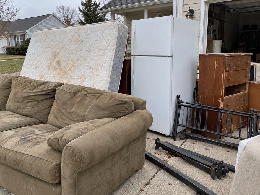 Discarded couch, stained mattress, refrigerator, dresser and bed frame set out on a suburban driveway